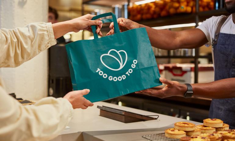 Un commerçant donne un sac avec le logo Too Good To Go à un client