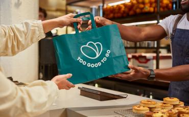 Un commerçant donne un sac avec le logo Too Good To Go à un client